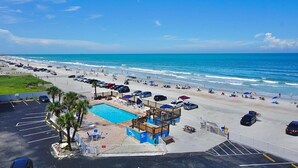A beachside view with a swimming pool, beach umbrellas, and a lifeguard tower. - OCEAN VIEW Studio@Daytona Zzz 4 (Daytona Beach)
