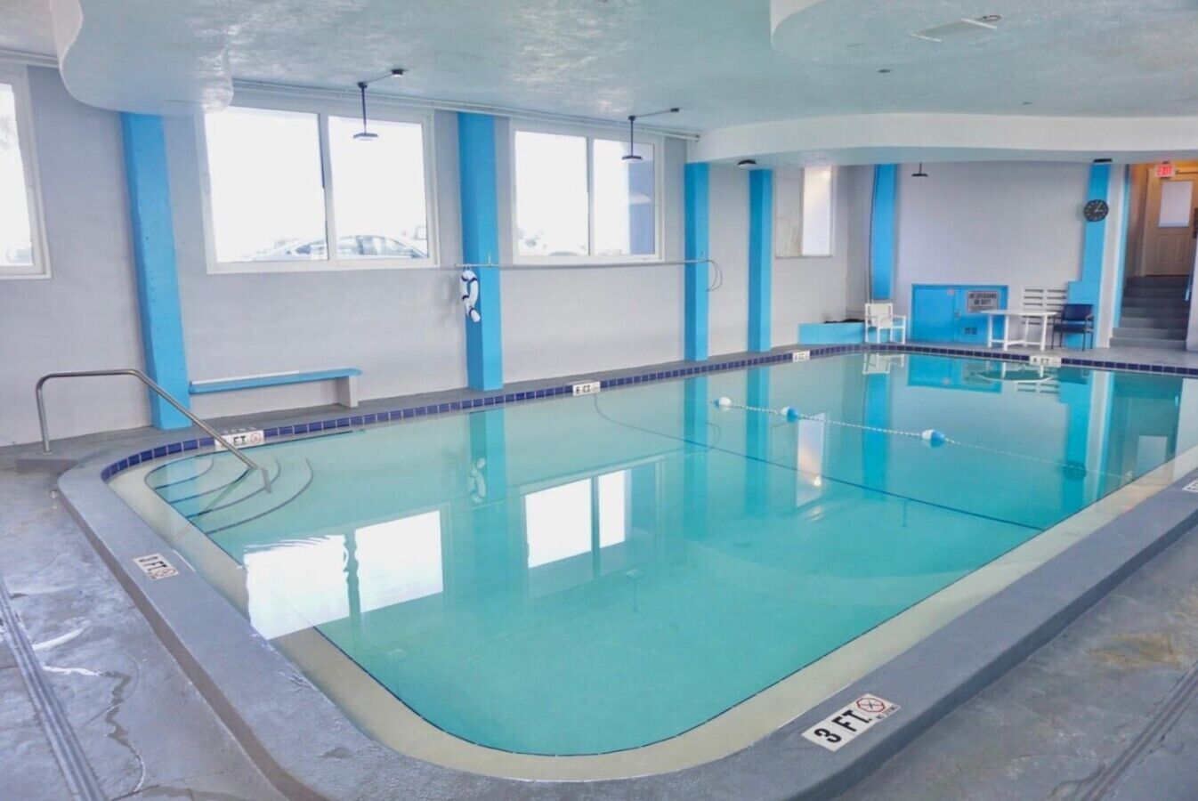 An indoor swimming pool with clear water, a diving board, and a lifeguard chair.