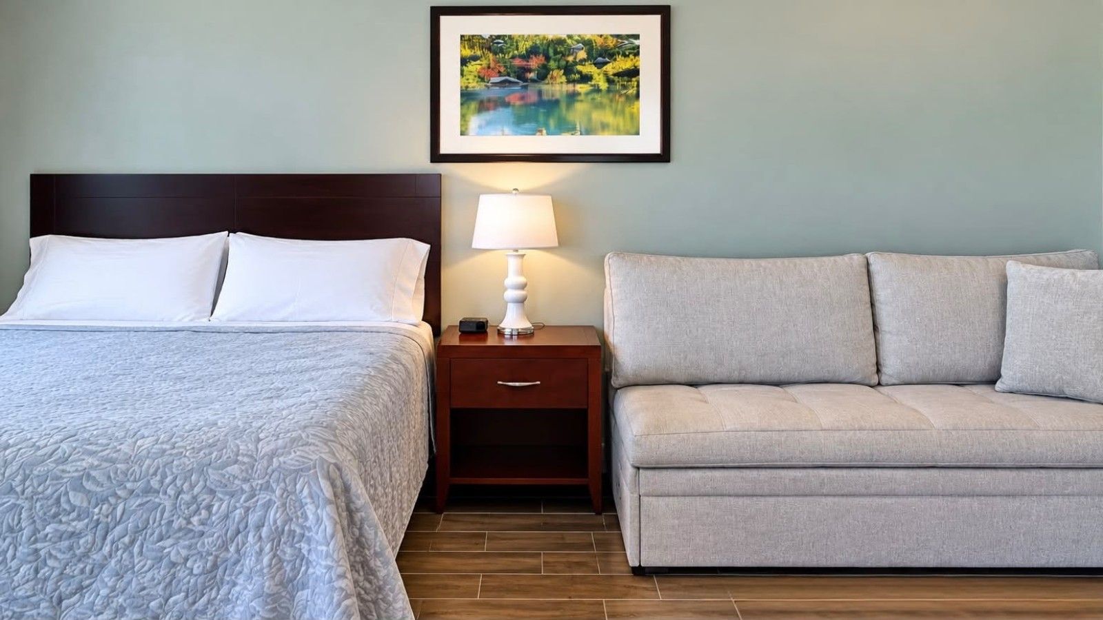Une chambre d’hôtel avec un lit, une table de chevet avec une lampe et un canapé.