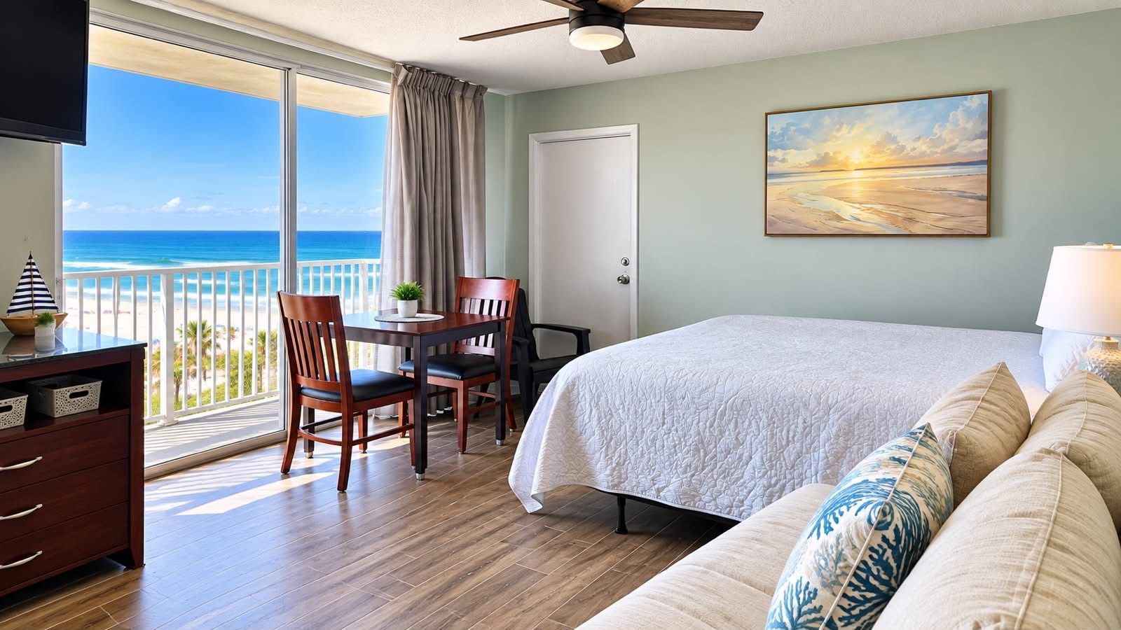 A hotel room with a balcony, a bed, a desk, and a television.