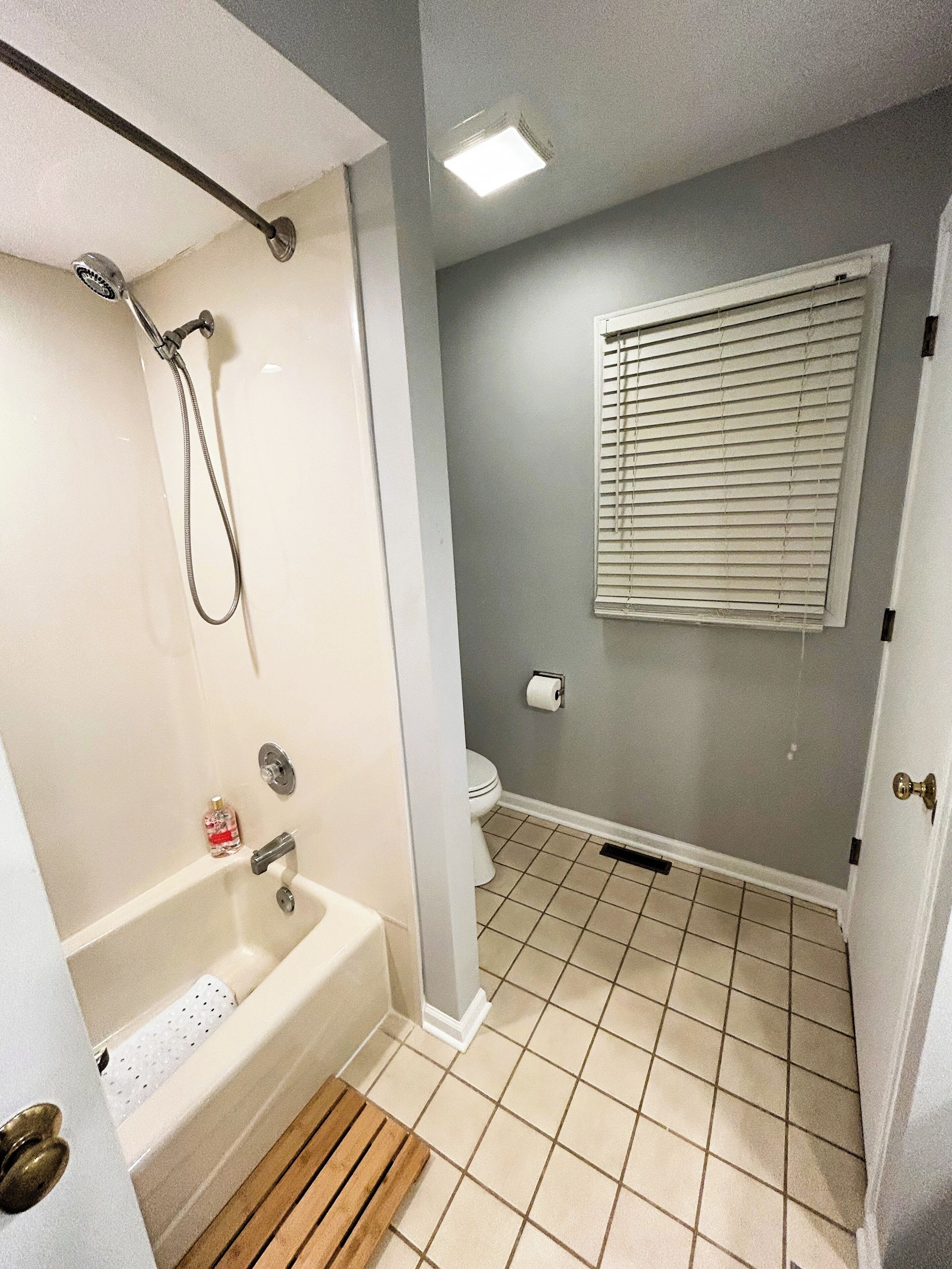Un baño con bañera, inodoro y ventana con persianas.