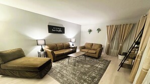 A living room with a sofa, two armchairs, a coffee table, and a rug. There is a sign on the wall and a ladder in the corner. - 6 Kings Ping-Pong Gazebo! (Northbrook)
