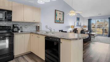 A modern kitchen with a dishwasher, stove, and coffee maker. There is a dining area with a table and chairs, and a balcony with a view.