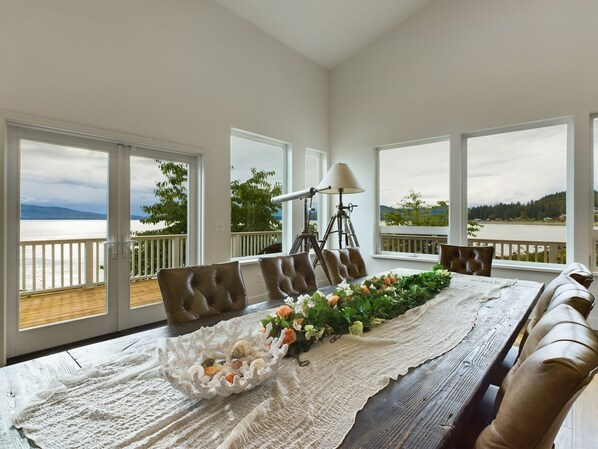 A dining area with a long table, multiple chairs, and a scenic view through large windows.