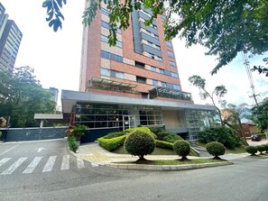Contemporary building with a glass facade and covered entrance, set amidst well-maintained landscaping.