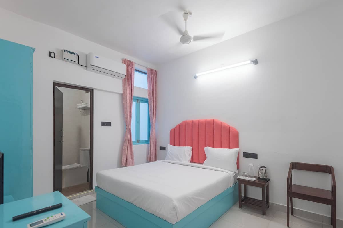 A bedroom with a bed, a nightstand, a chair, a bathroom with a shower, and a ceiling fan.
