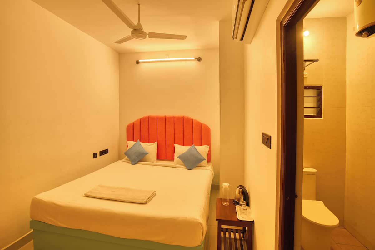 A hotel room with a bed, a ceiling fan, a bedside table, and a bathroom with a toilet and sink.
