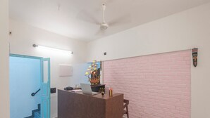 A reception area with a brown counter, a laptop, a decorative ship model, and a pink brick wall. - Daffodils by La Maison Charu  (Puducherry)