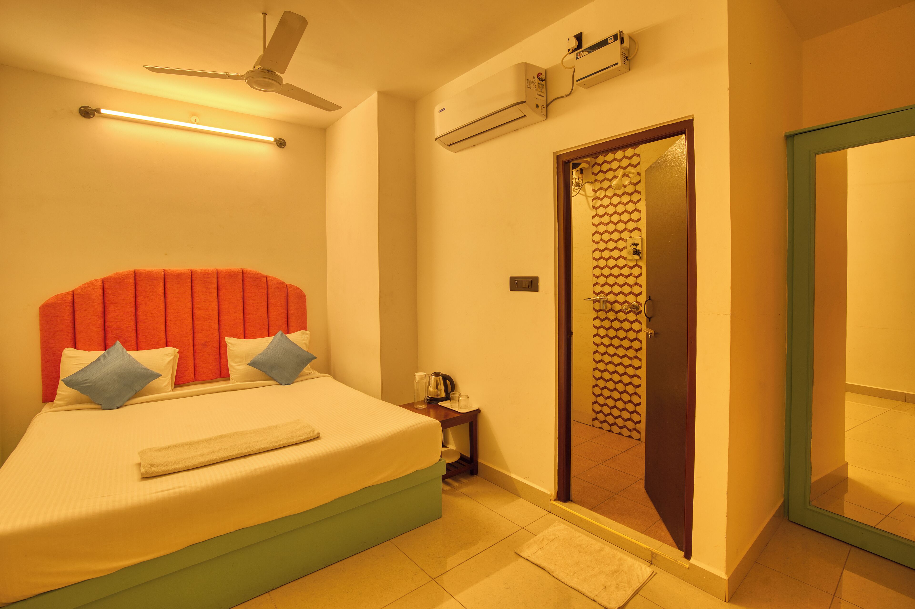 A hotel room with a bed, a nightstand, an air conditioning unit, a ceiling fan, and a door with a patterned design.