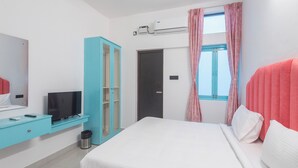 A modern hotel room with a bed, a TV, a wardrobe, and a window with curtains. - Daffodils by La Maison Charu  (Puducherry)