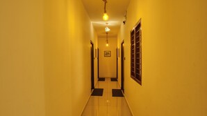 A narrow hallway with a tiled floor and yellow walls. There are two doors on either side and a light fixture hanging from the ceiling. - Daffodils by La Maison Charu  (Puducherry)