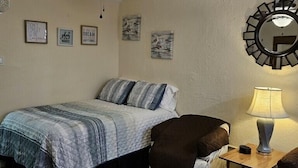 Quarto com cama, poltrona, luminária, ventilador de teto e obras de arte nas paredes.