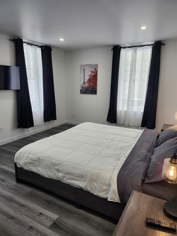 A modern bedroom with a large bed, black curtains, a mounted TV, and a painting of the Eiffel Tower.