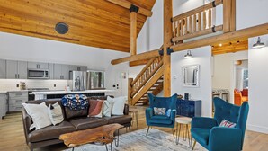 Een ruime woonkamer met een houten plafond, een bruine leren bank, teal fauteuils en een houten salontafel.