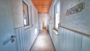 A narrow hallway with wooden ceiling beams, white textured walls, and a tiled floor. - Good prices Good travel, 4 bedrooms and 2 bathrooms on 130sqm (Neuried)