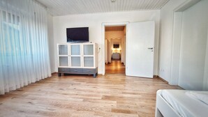 A room with wooden flooring, a white cabinet with glass doors, a television on top, and a door leading to another room. - Good prices Good travel, 4 bedrooms and 2 bathrooms on 130sqm (Neuried)