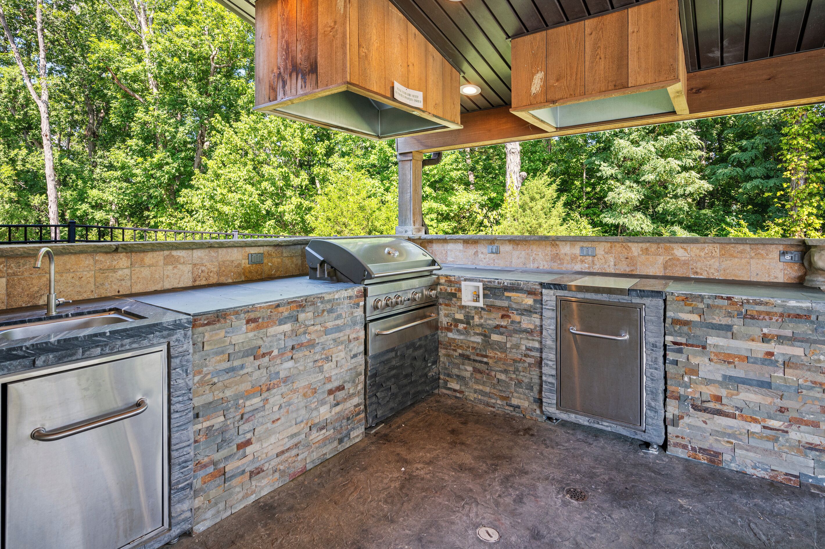 An outdoor kitchen with a built-in grill, stone backsplash, and wooden cabinets.