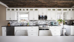 Una cocina moderna con armarios blancos, protector contra salpicaduras de piedra y techo de madera.