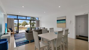 A modern living room with a dining area, large windows, and a beach-themed painting.