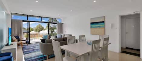 A modern living room with a dining area, large windows, and a beach-themed painting.
