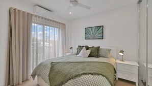 A bedroom with a bed, two bedside tables, a ceiling fan, and a window with curtains.