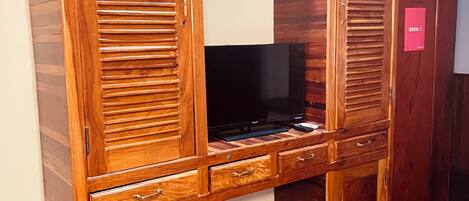 A wooden wardrobe with multiple compartments and a flat-screen TV.