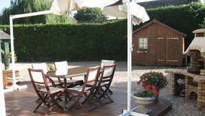 Eine Holzterrasse mit Tisch, Stühlen, einem weißen Sonnenschirm und einem gemauerten Grill.