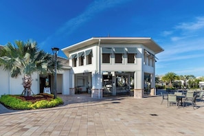 A building with a covered patio area, outdoor seating, and a landscaped garden with palm trees. - Luxury Private Pool Townhouse/Free Water Park/5B4B (Kissimmee)