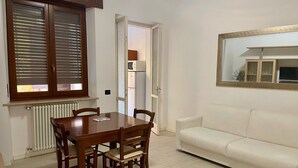 A dining area with a wooden table and chairs, a white sofa, and a window with blinds. - INTERO APPARTAMENTO NEL CUORE DEL CENTRO STORICO DI VERONA (Verona)