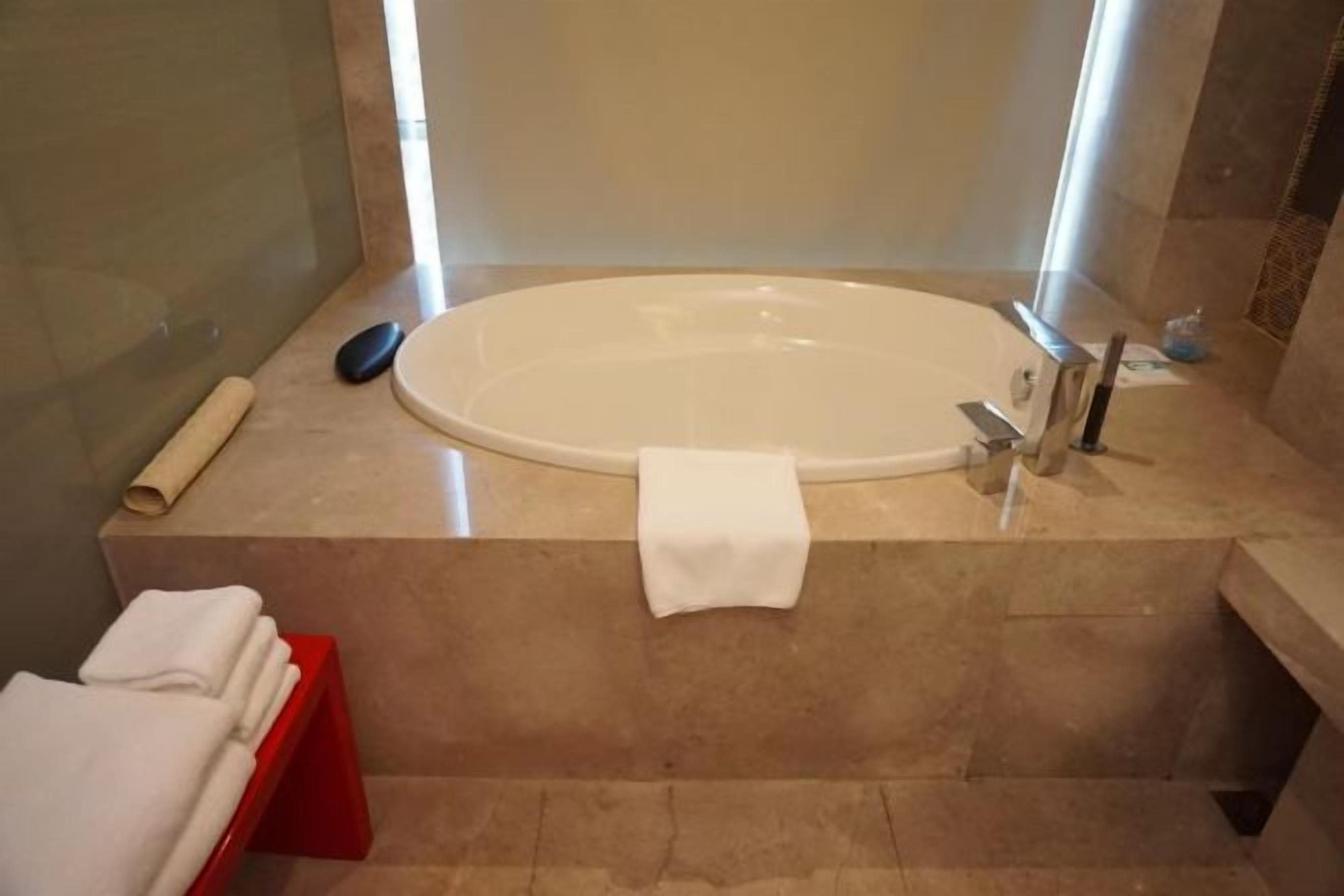 Uma casa de banho com uma banheira grande, um porta-toalhas vermelho e uma toalha branca no chão.