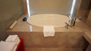 Uma casa de banho com uma banheira grande, um porta-toalhas vermelho e uma toalha branca no chão.