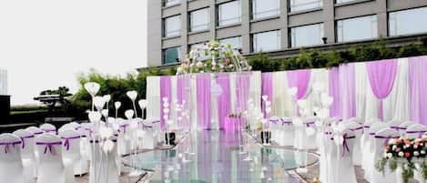 En tagterrasse med swimmingpool i glas, indretning i hvidt og lilla, og baggrund med blomsterdekorationer.
