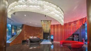 Um lobby moderno com uma receção curva, um candelabro grande e uma área de estar vermelha.