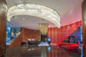 Un hall d’entrée moderne avec un comptoir d’accueil incurvé, un grand lustre et un espace détente rouge.