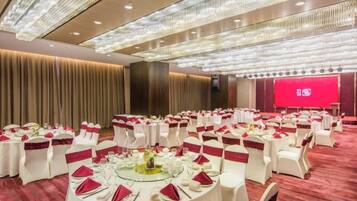 Un salón de banquetes con mesas redondas, sillas blancas y cintas rojas.