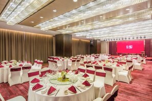 Une salle de banquet avec des tables rondes, des chaises blanches et des rubans rouges.