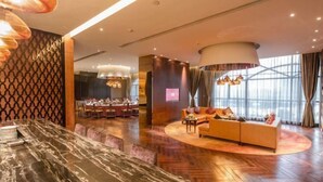 A modern hotel lobby with a marble reception desk, a dining area, and a seating area with a sofa and lamps. - Joyc Hotel Dongguan (Dongguan)