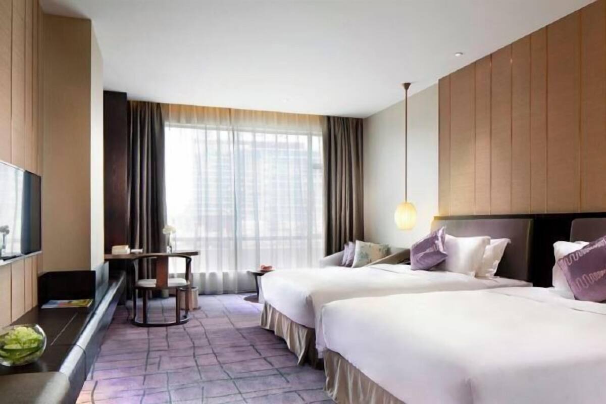 Een hotelkamer met twee bedden, een bureau, een stoel en een groot raam met gordijnen.