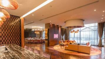 A modern hotel lobby with a marble reception desk, a dining area, a sofa, and a large window with curtains.