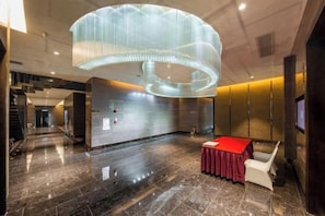 Een ruime lobby met een moderne kroonluchter, een receptiebalie en een zithoek.