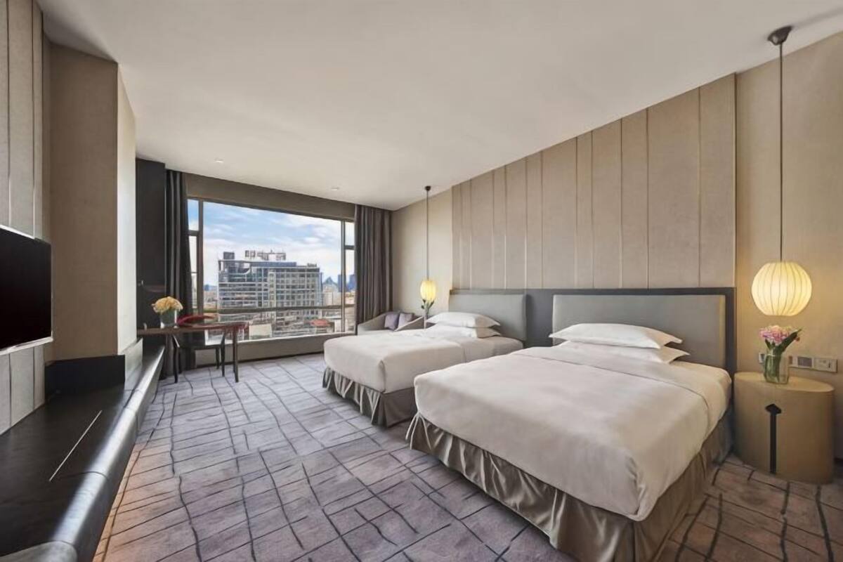 Een hotelkamer met twee bedden, een televisie, een bureau en een groot raam met uitzicht op de stad.