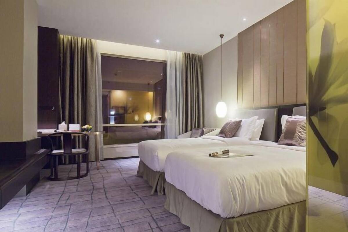 Een hotelkamer met twee bedden, een bureau met een stoel en een groot raam met gordijnen.