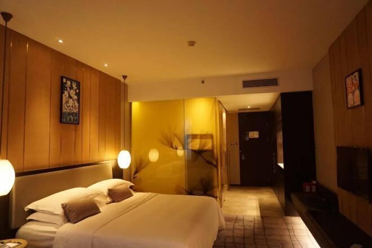 Een hotelkamer met een bed, bedlampen, een spiegel, een deur en een aan de muur bevestigde televisie.