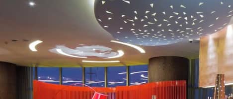 Un moderno vestíbulo con techo curvo, separador rojo y zona de bar.