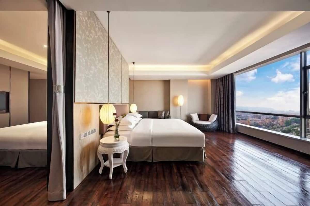 Een moderne hotelkamer met een groot bed, een nachtkastje met een lamp, een stoel en uitzicht op de stad.