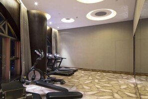 Une salle de sport équipée de divers appareils, notamment des tapis de course et un vélo elliptique, dans une pièce dont le sol est décoré de motifs et qui est éclairée par un système d’éclairage moderne.