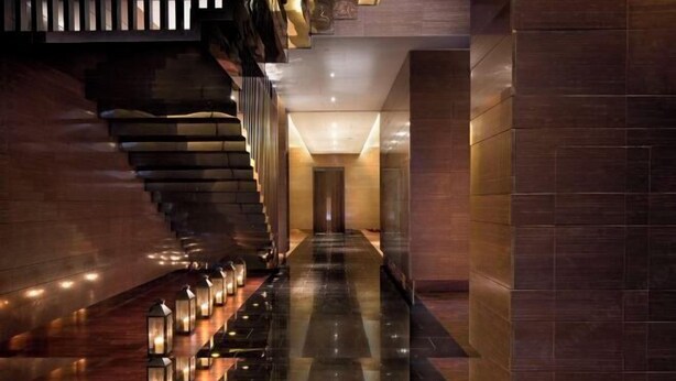 A modern hotel lobby with a reflective floor, a staircase with wooden railings, and a series of wall-mounted lights. - Joyc Hotel Dongguan (Dongguan)