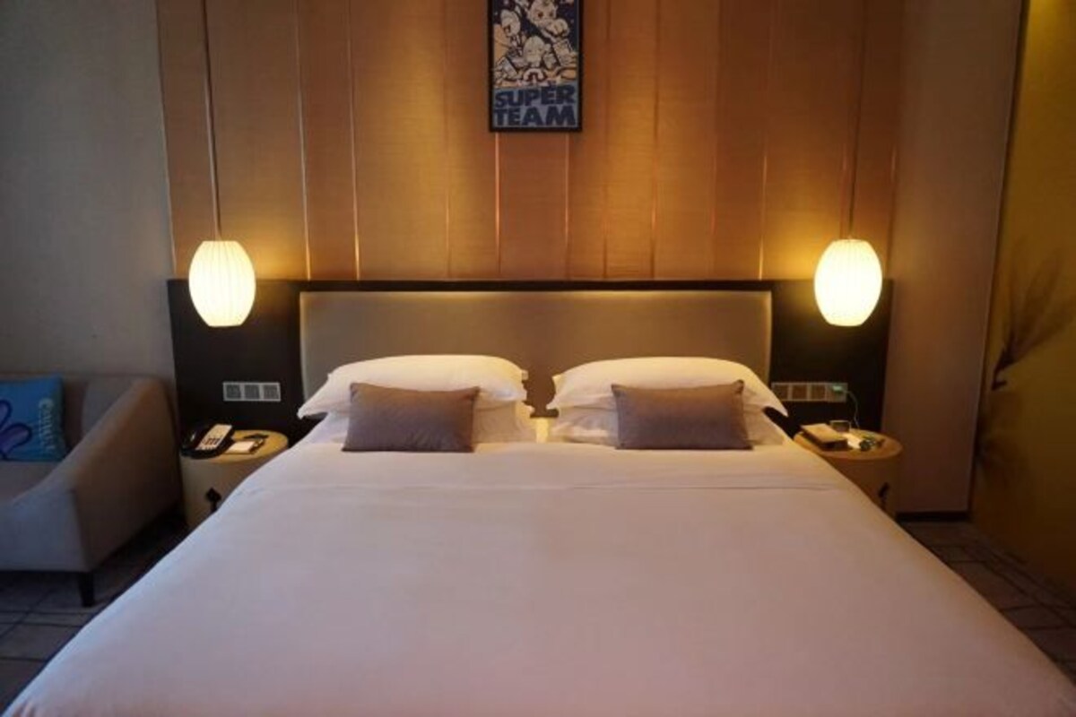 Une chambre d’hôtel avec un grand lit, deux lampes de chevet, une œuvre d’art accrochée au mur et une petite table sur laquelle se trouvent un téléphone et une lampe.