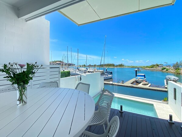 A patio with a table and chairs, overlooking a marina with boats and a clear blue sky.