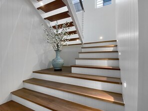 Un escalier avec des marches en bois et des murs blancs, un vase rempli de fleurs et une lucarne.